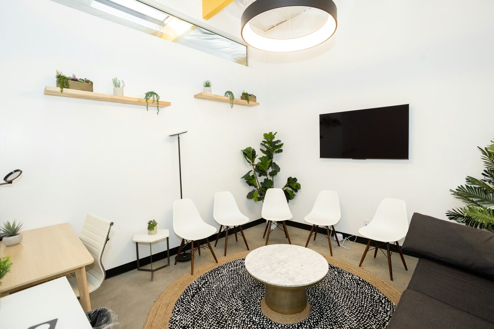 A bright waiting room with white chairs, a round table and plants